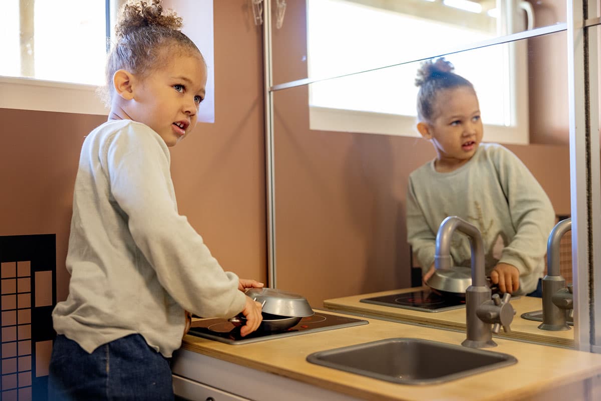 Lite barn leker ved en lekekomfyr og ser forsiktig mot siden