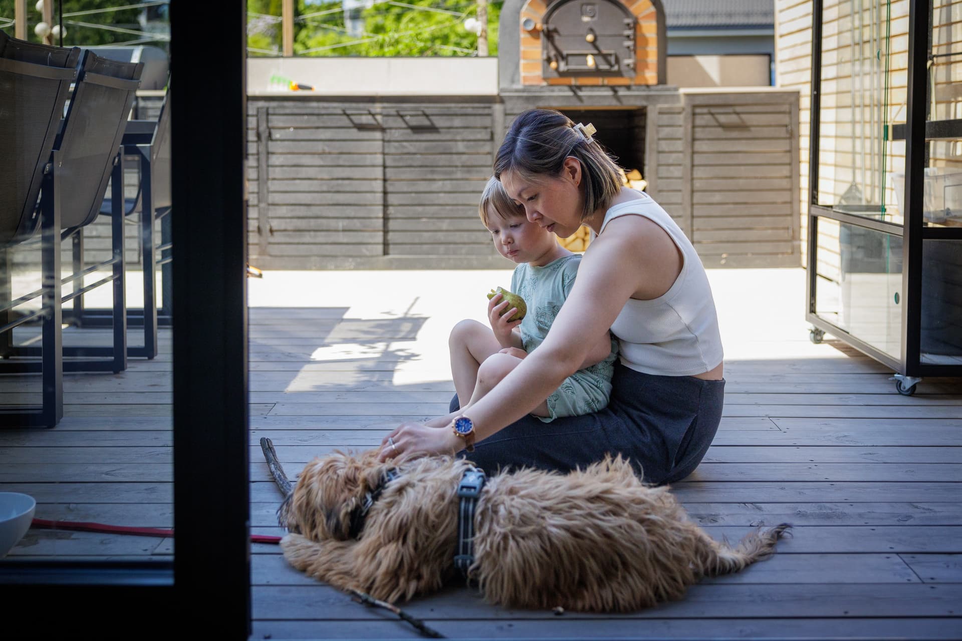 Voksen og lite barn sitter på en terrasse og klapper en hund