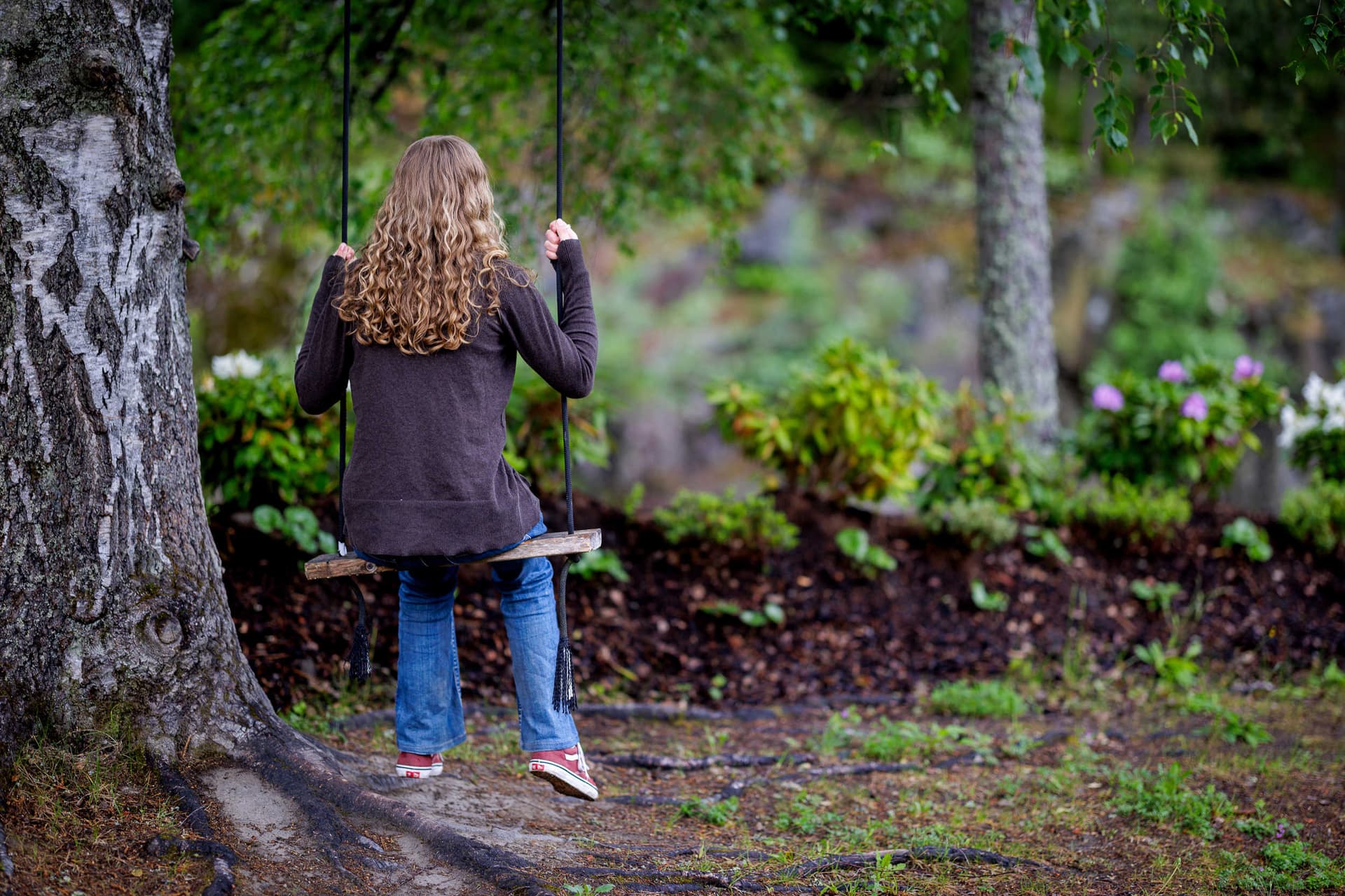 Barn som sitter på en huske under et tre, omgitt av grønn hage