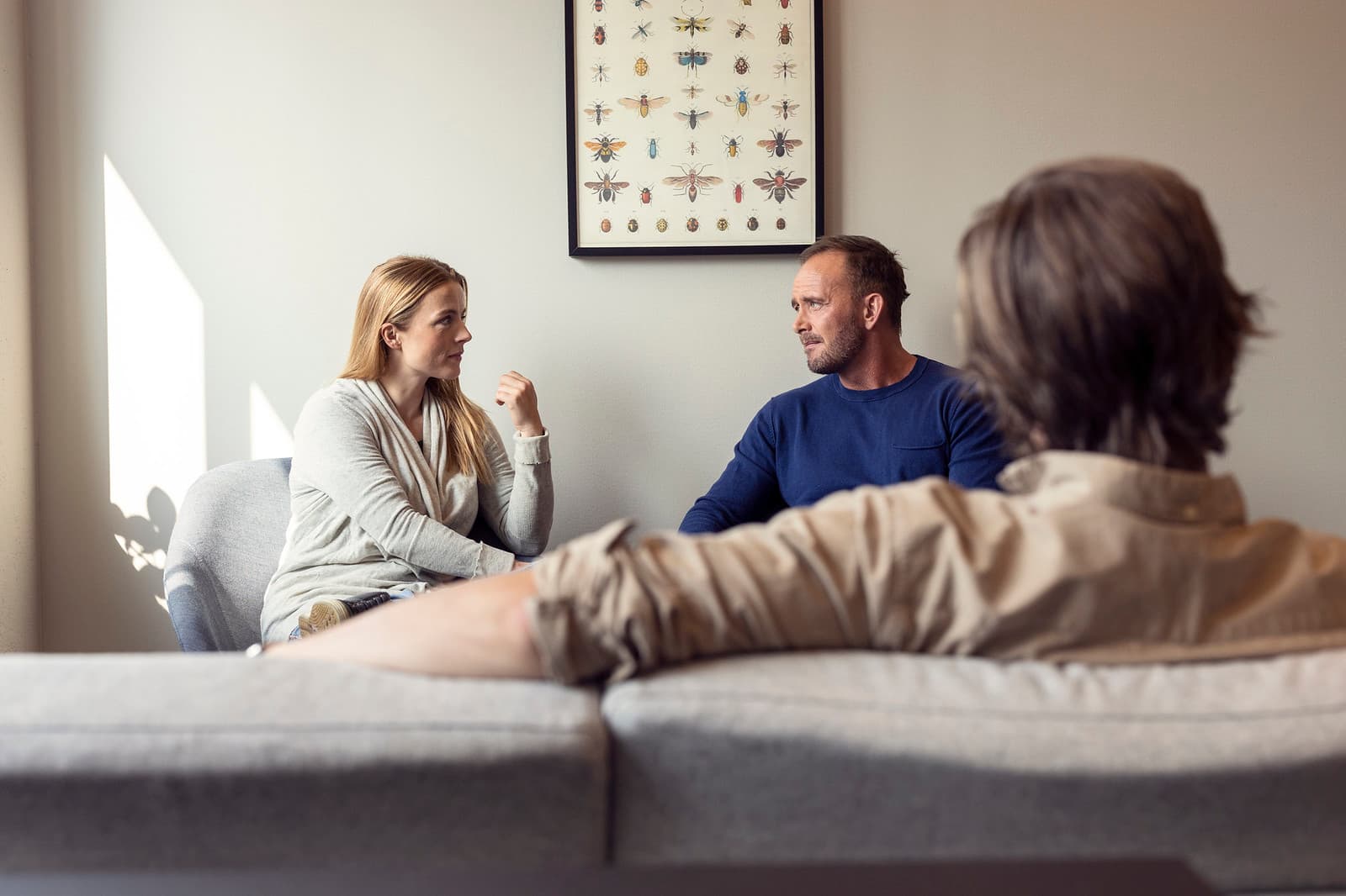 To voksne mennesker som sitter i en sofa, foran dem sitter en tredje voksen. 
