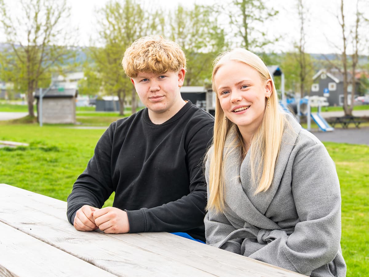 To unge voksne, en gutt og en jente, sitter på en benk utendørs