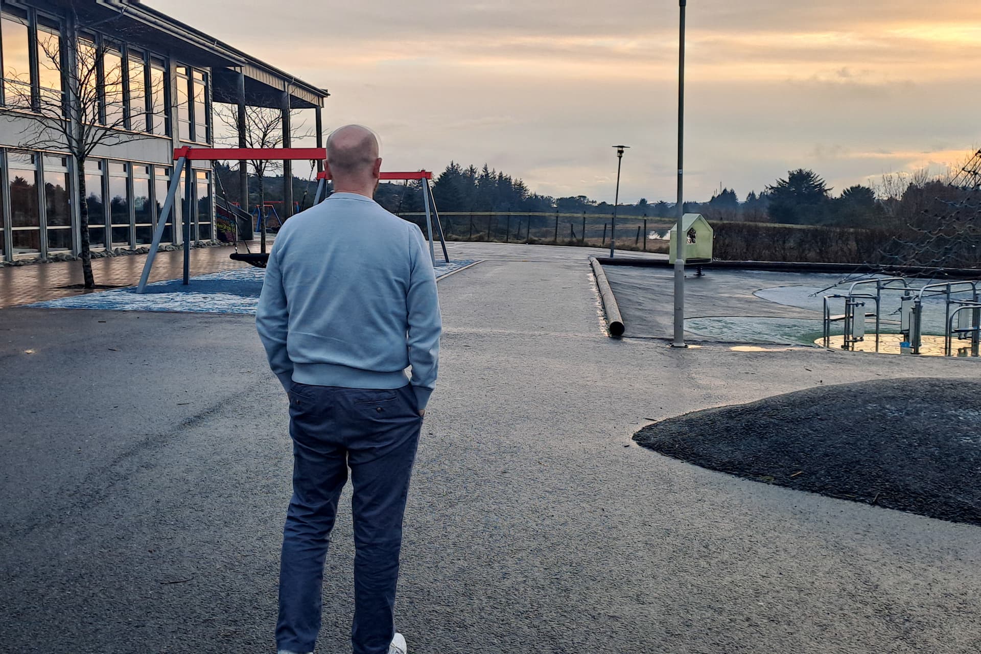 Fosterfar fra Karmøy står i en skolegård med ryggen til