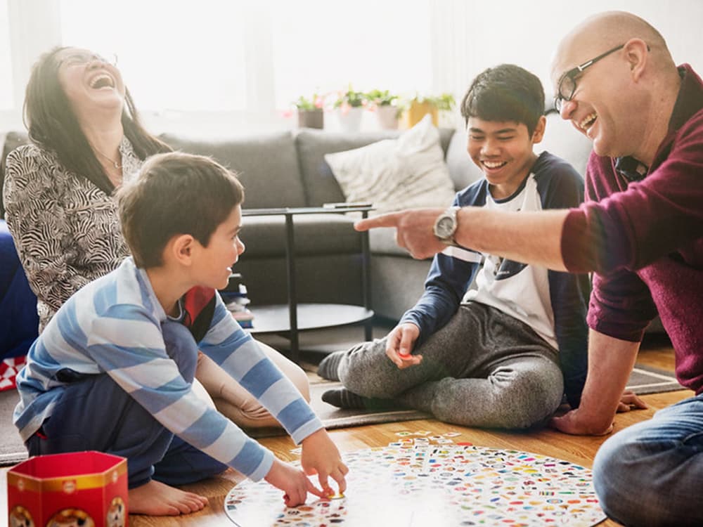 En familie på fire personer sitter på gulvet, spiller et spill og ler sammen