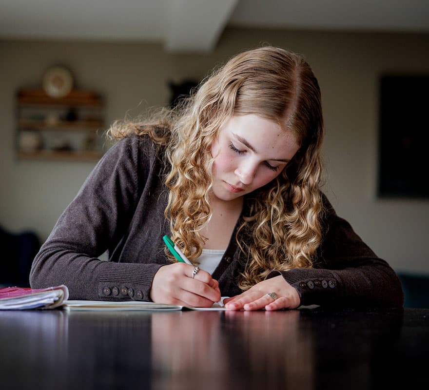 Ung jente sitter ved et bord hjemme og gjør lekser