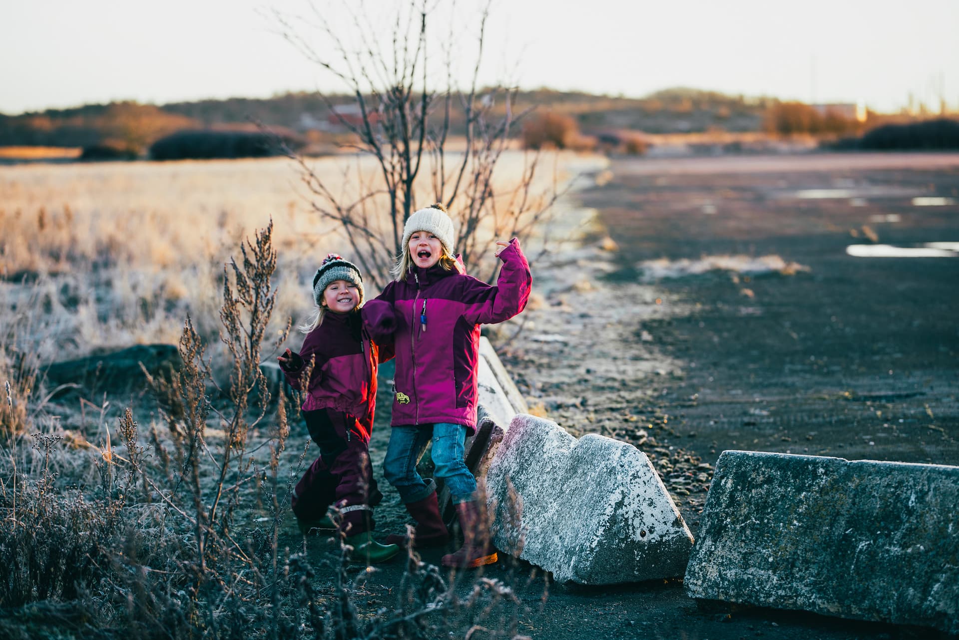 To barn smiler og jubler på en grusbane. De har på seg vårjakker og luer
