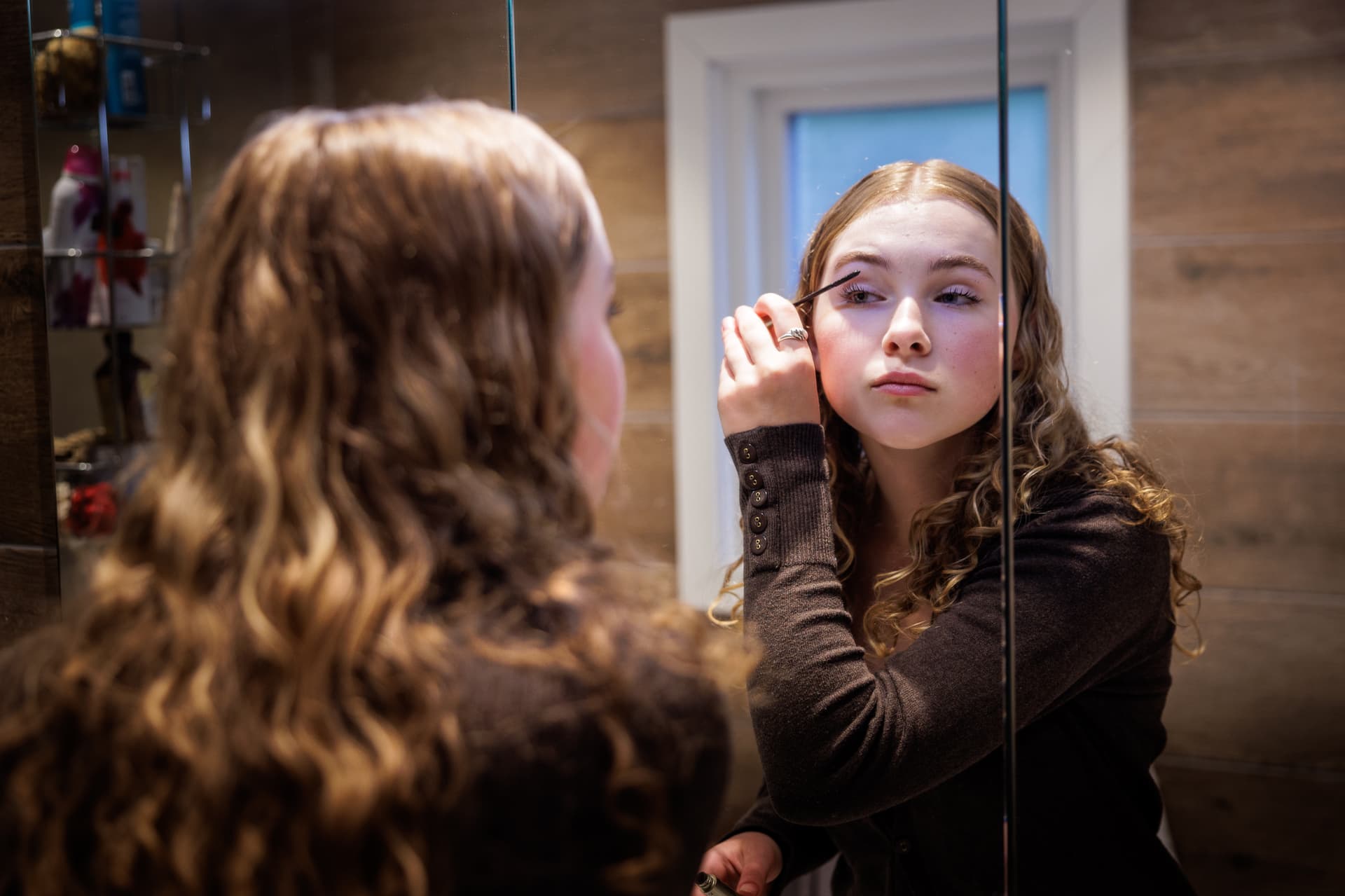 Ung person som står foran et baderomsspeil og tar på mascara.