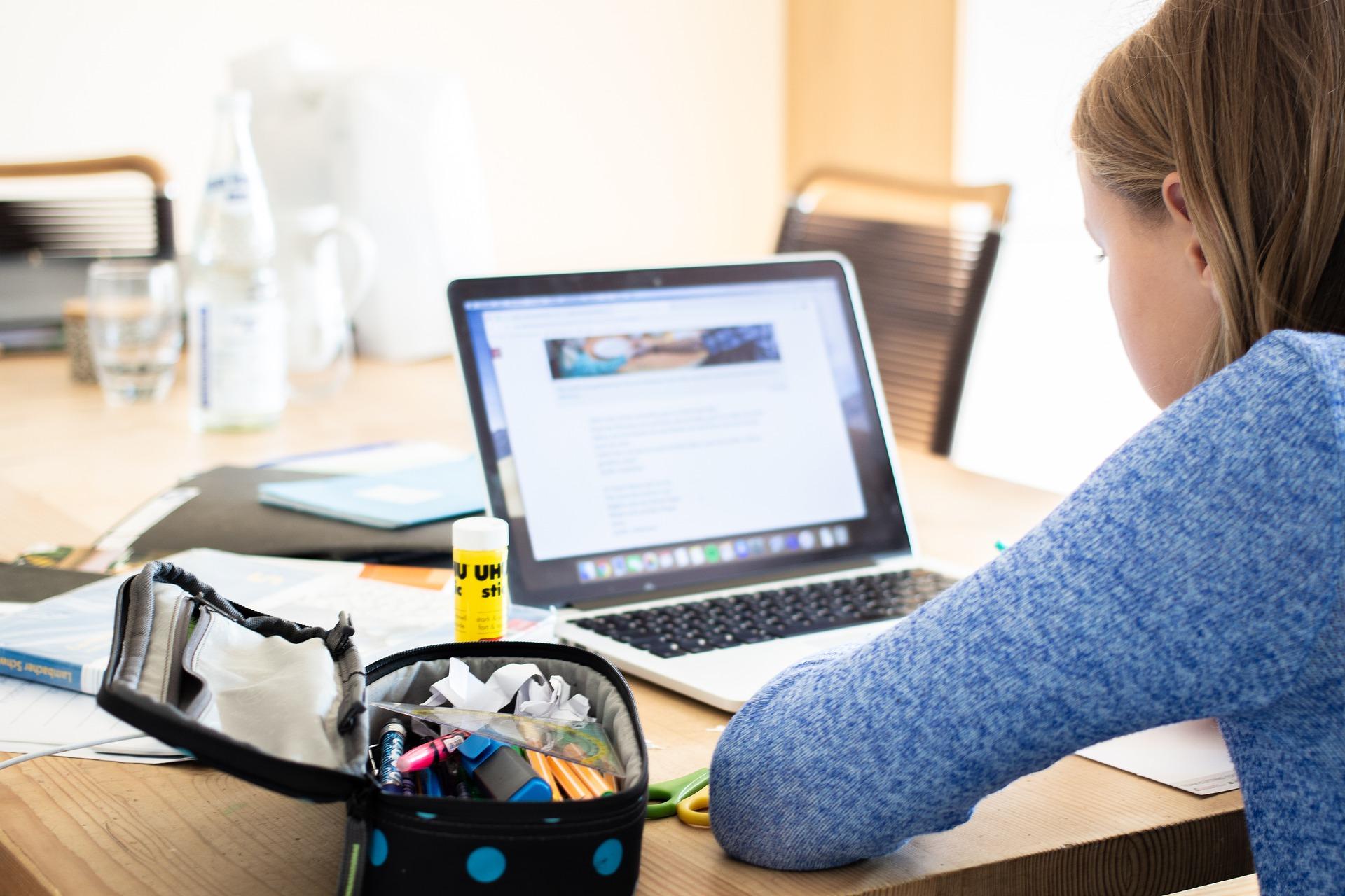 Jente som sitter og leser på en pc-skjerm med et åpent penal og skrivesaker ved siden av seg