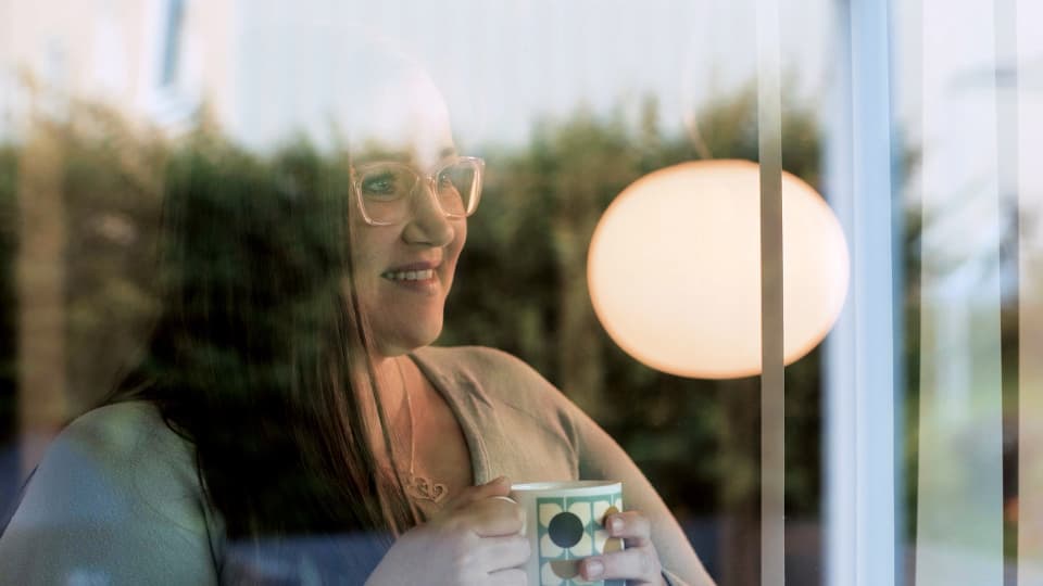 kvinne holder en kaffekopp og ser ut vindu