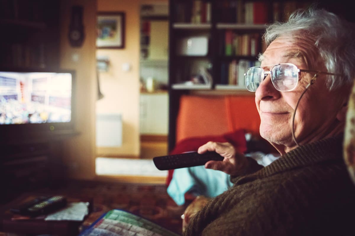 eldre person sit i stova og ser på tv
