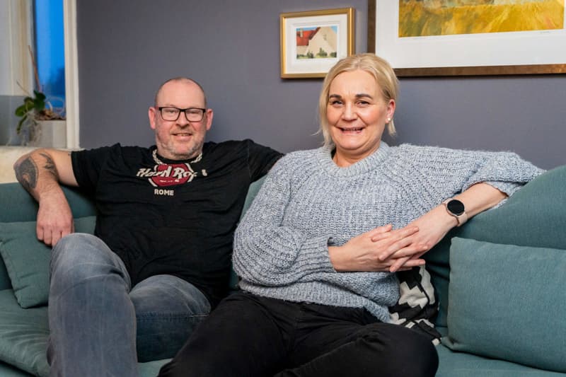 Tom og Gro sitter i sofaen og smiler mens de ser i kameraet.