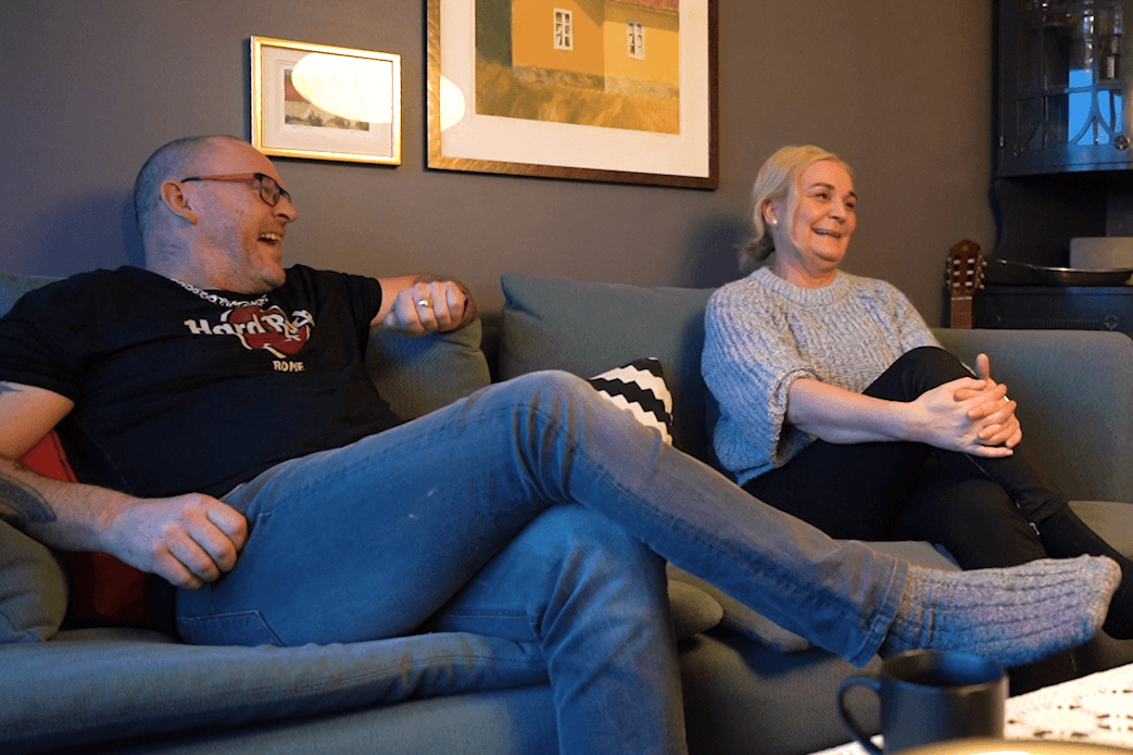 Gro og Tom sitter i sofaen og ser i kameraet.