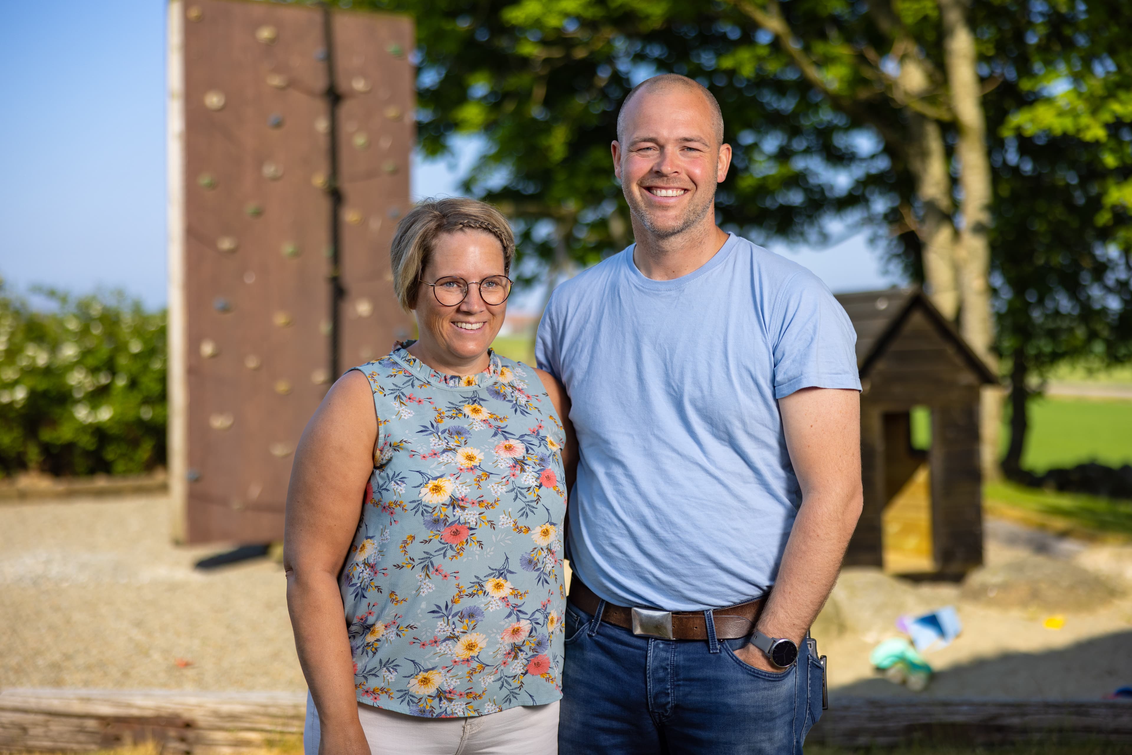 Ektepar står foran en lekeplass, holder rundt hverandre og smiler til kameraet.