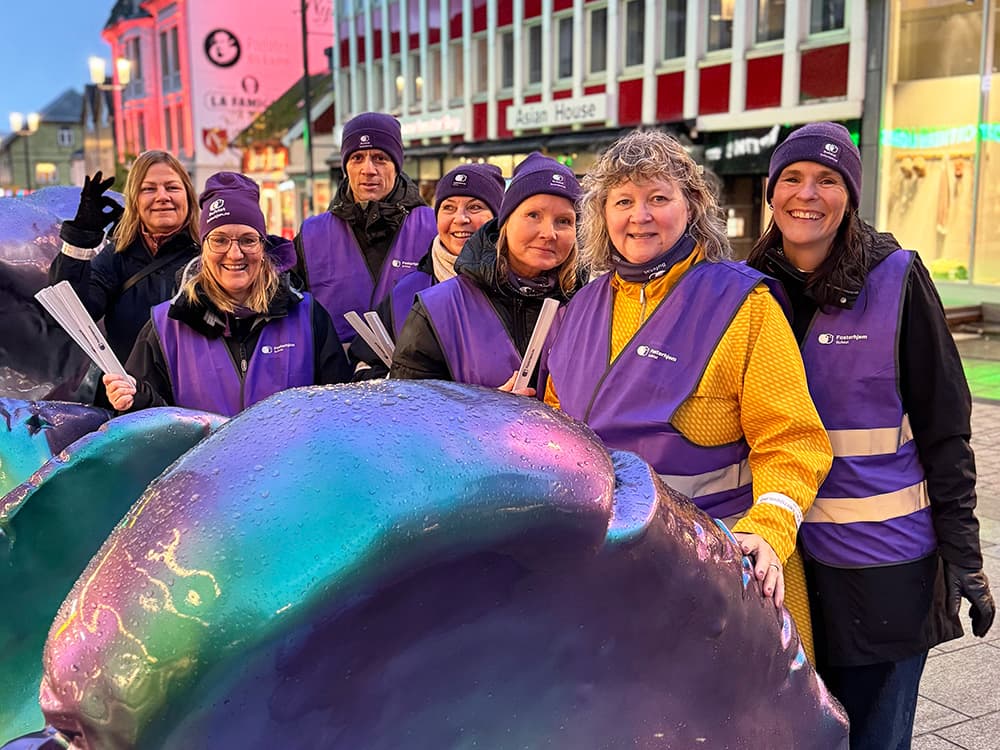 Rådgivere i fosterhjemstjenesten ikledd lilla refleksvester, står bak et kunstmonument