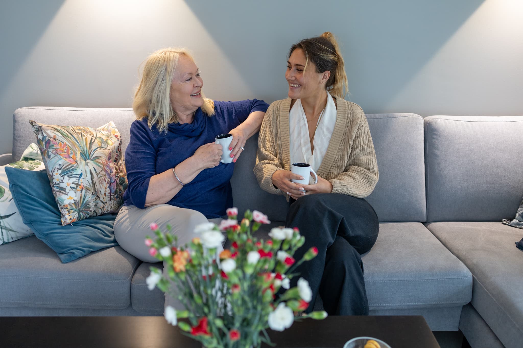 Fostermor og fosterdatter smiler til hverandre sittende i sofa