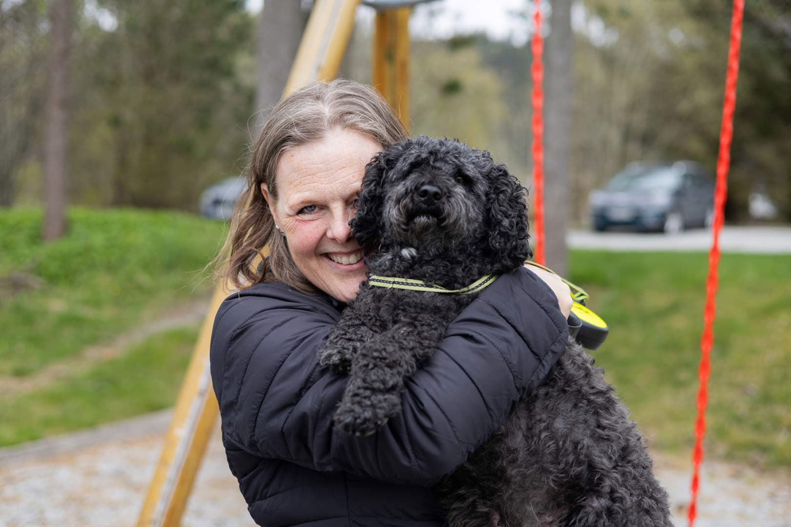 dame løfter hund mens hun smiler på en lekeplass