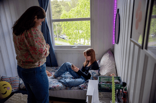 Mor på rommet til datteren som sitter i senga med telefonen