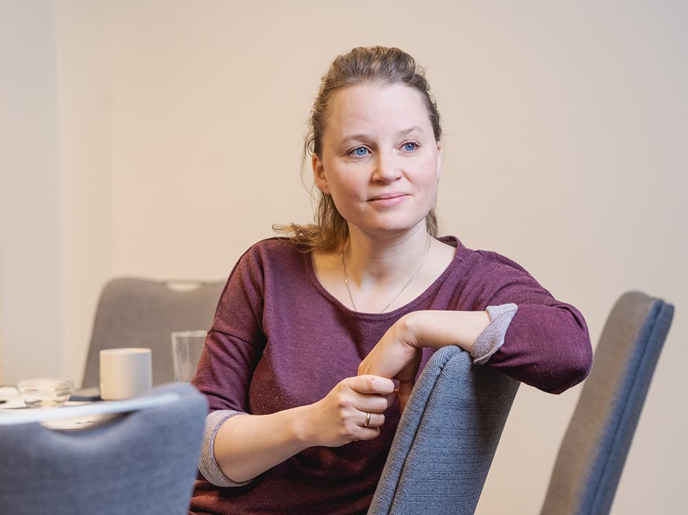 En kvinne sitter på en stol og lener armen på ryggstøtten