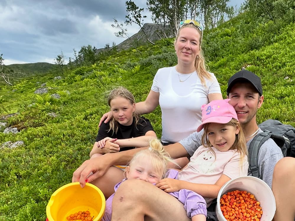 To foreldre og tre barn sitter i grønn lyng med multebær i bøtter