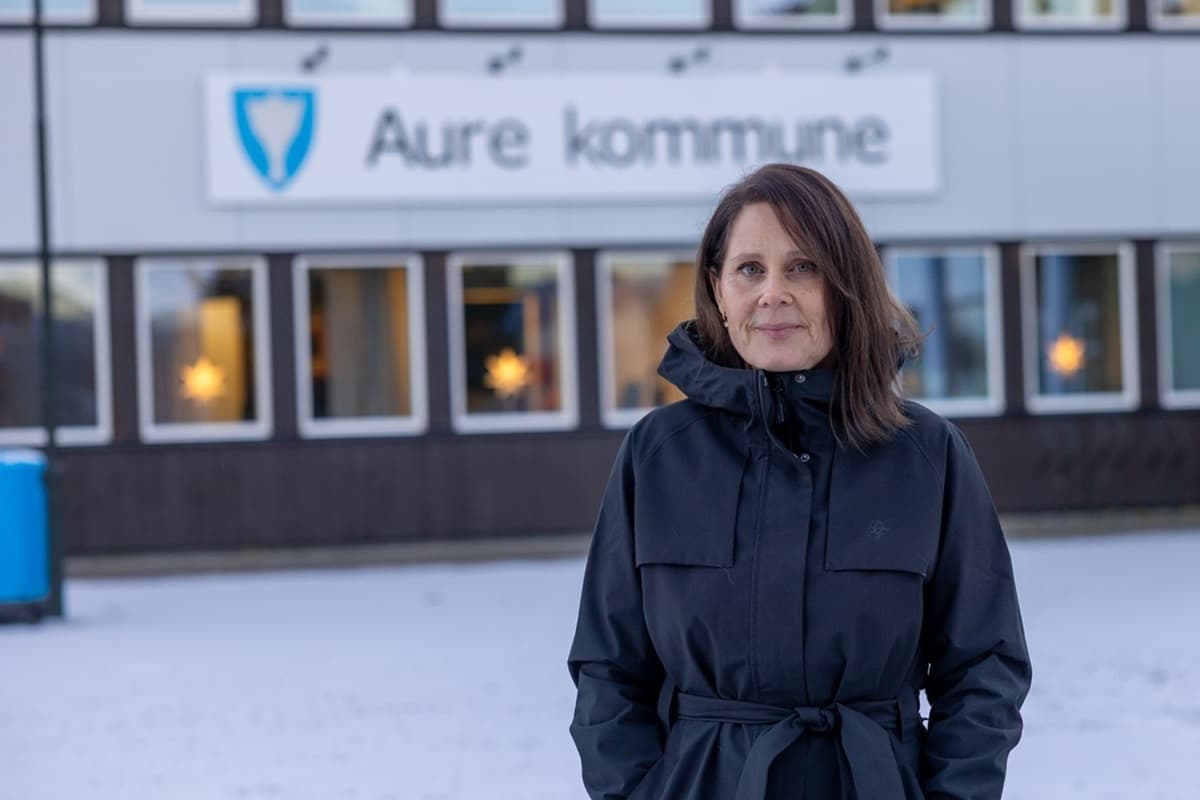 May-Britt Nordgård står foran en bygning som har skilt med kommunevåpen og tekst Aure kommune