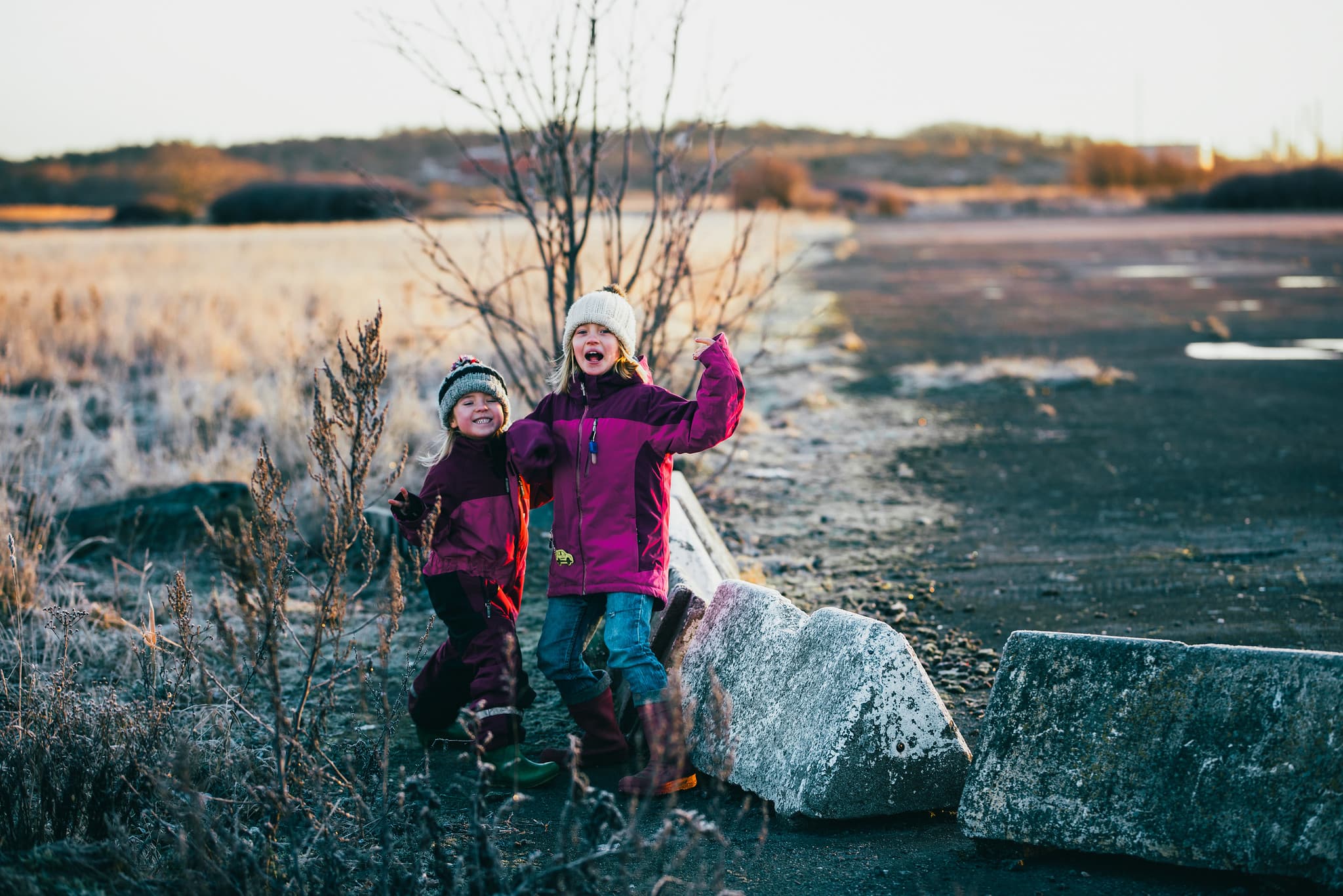 To barn smiler og jubler på en grusbane. De har på seg vårjakker og luer