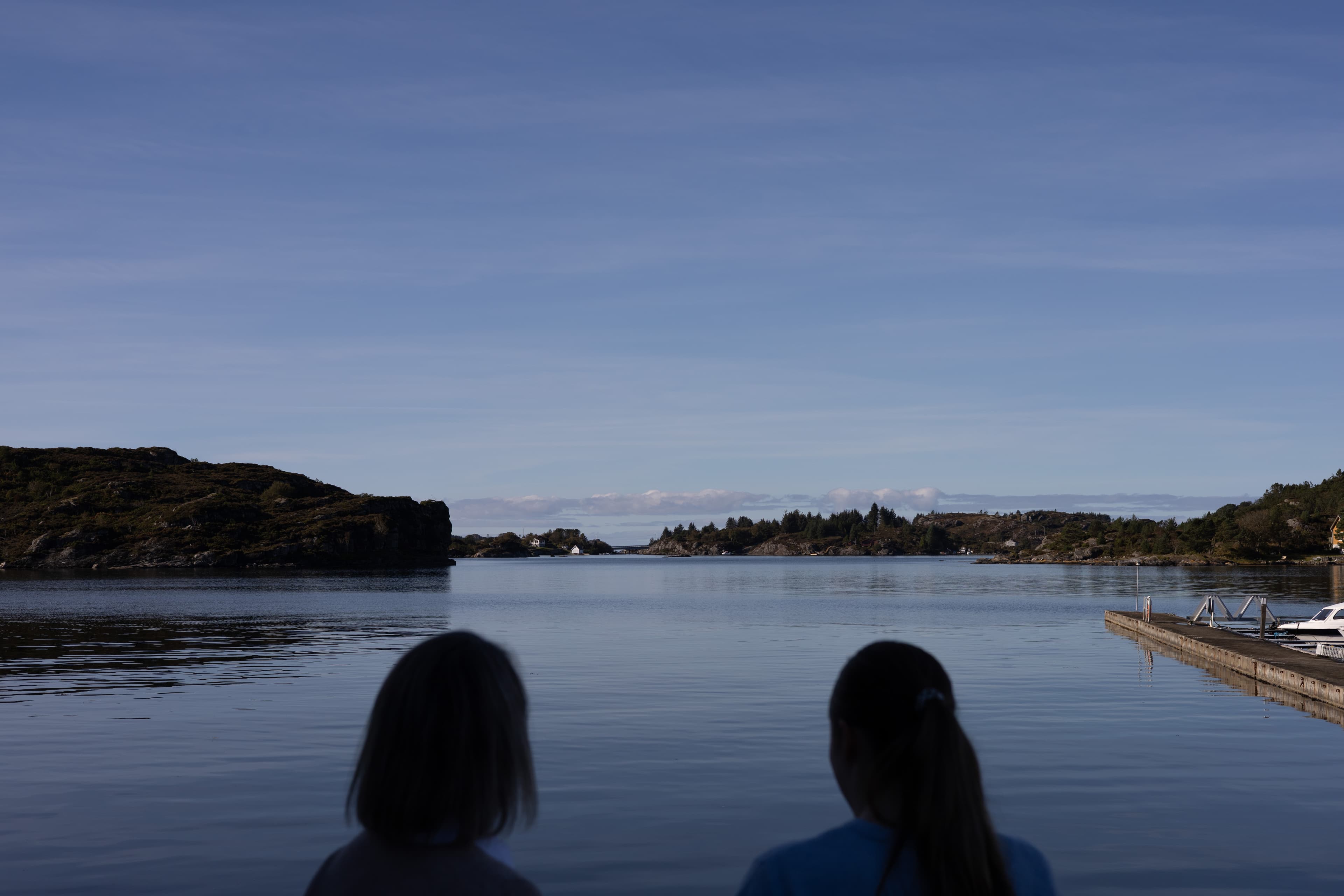 Siluett av to personer foran sjø og blå himmel