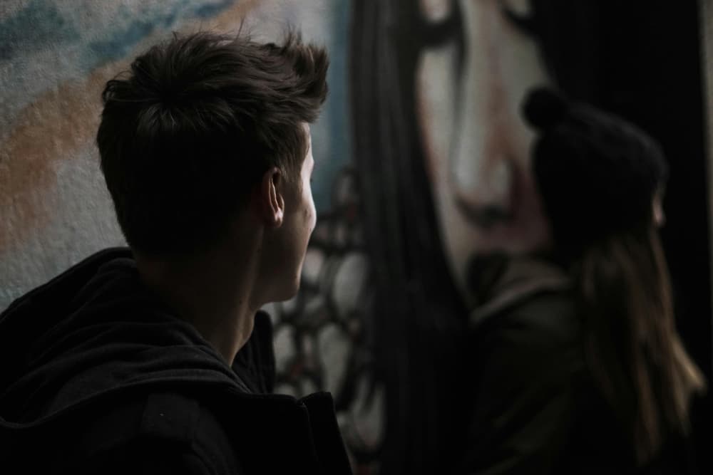 To ungdommer som sitter i mørket langs en vegg med grafitti