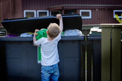 Barn kaster søppelpose i søppelkasse.