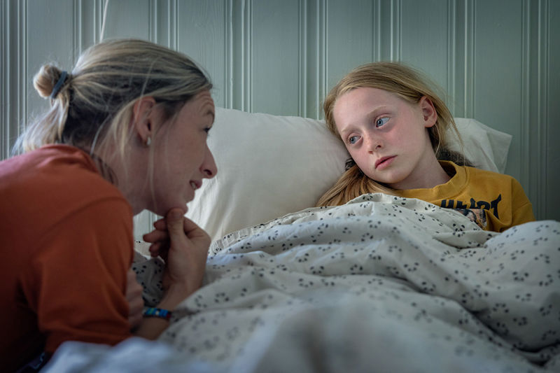 Mother talking to daughter lying in bed.