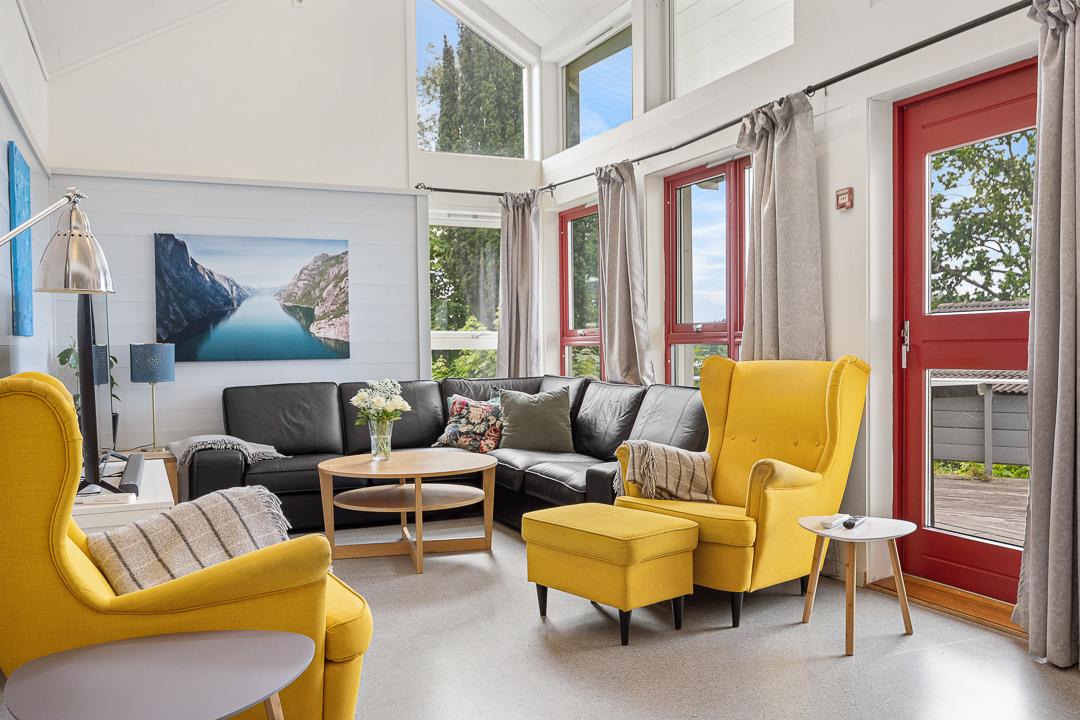 Stue med høyt tak, rød tør til terrasse, gule lenestoler og svart skinnsofa. 