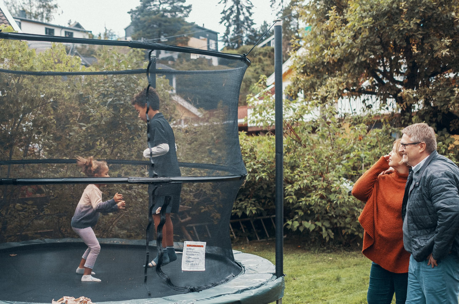 Bilde av to barn på trampoline, to voksne som ser på
