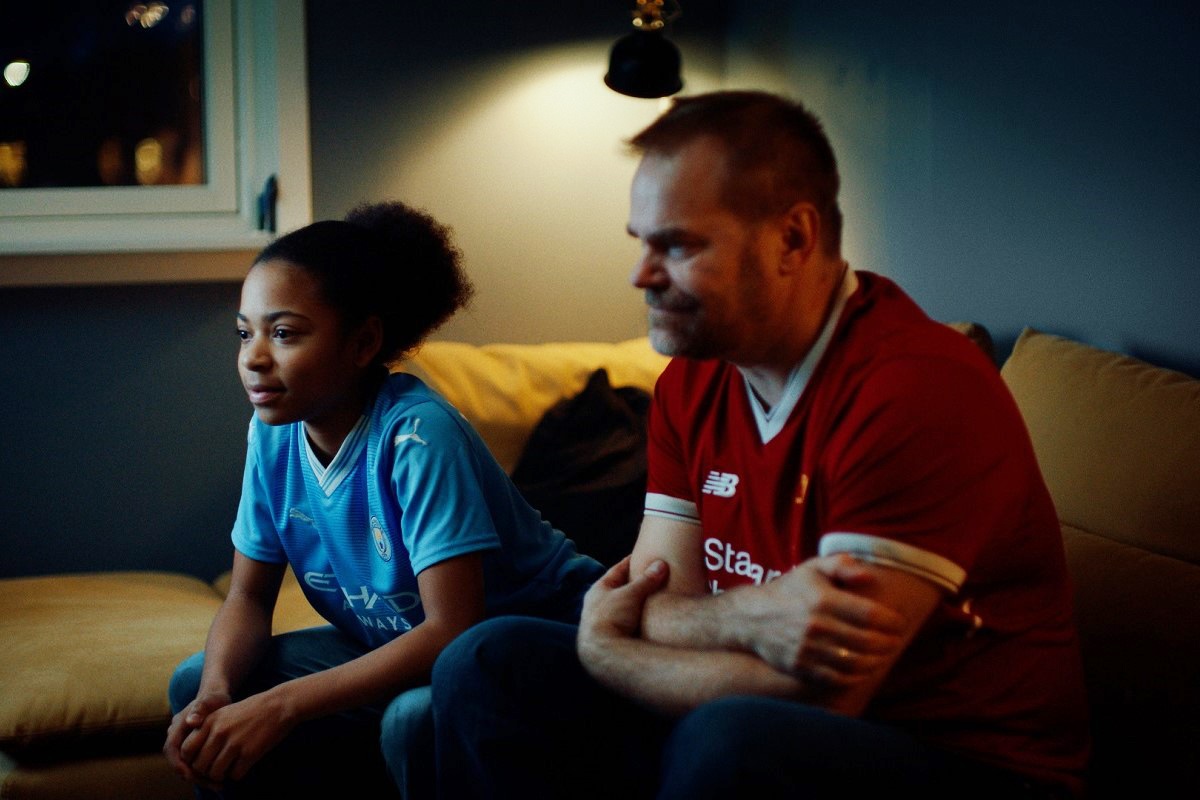 en jente og en mann sitter i sofa og ser på fotballkamp. illustrasjonsbilde